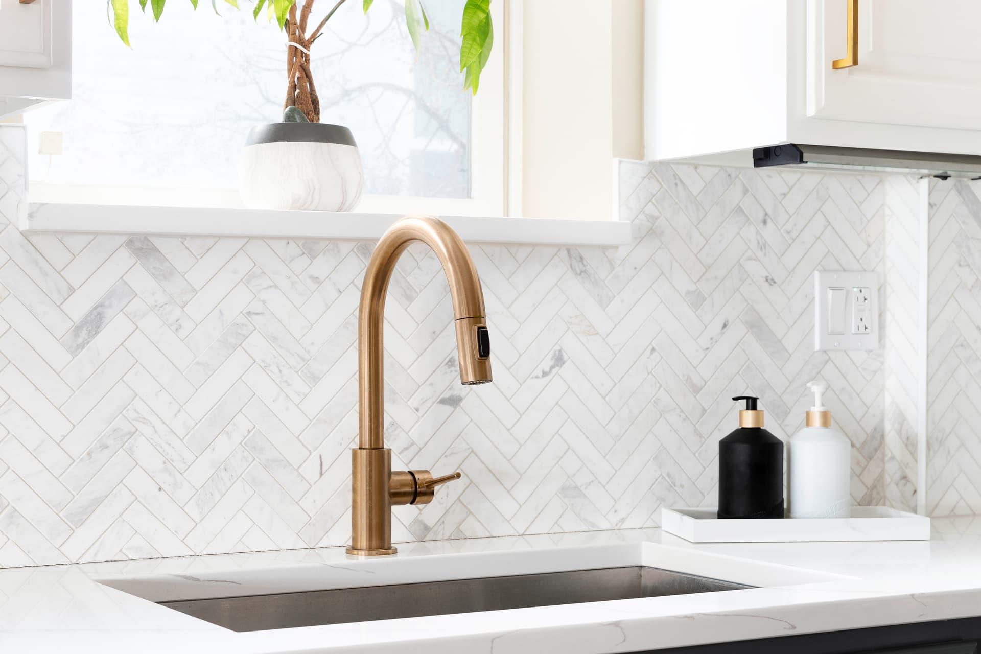 Brass pull-down faucet over an undermount sink with a marble herringbone backsplash