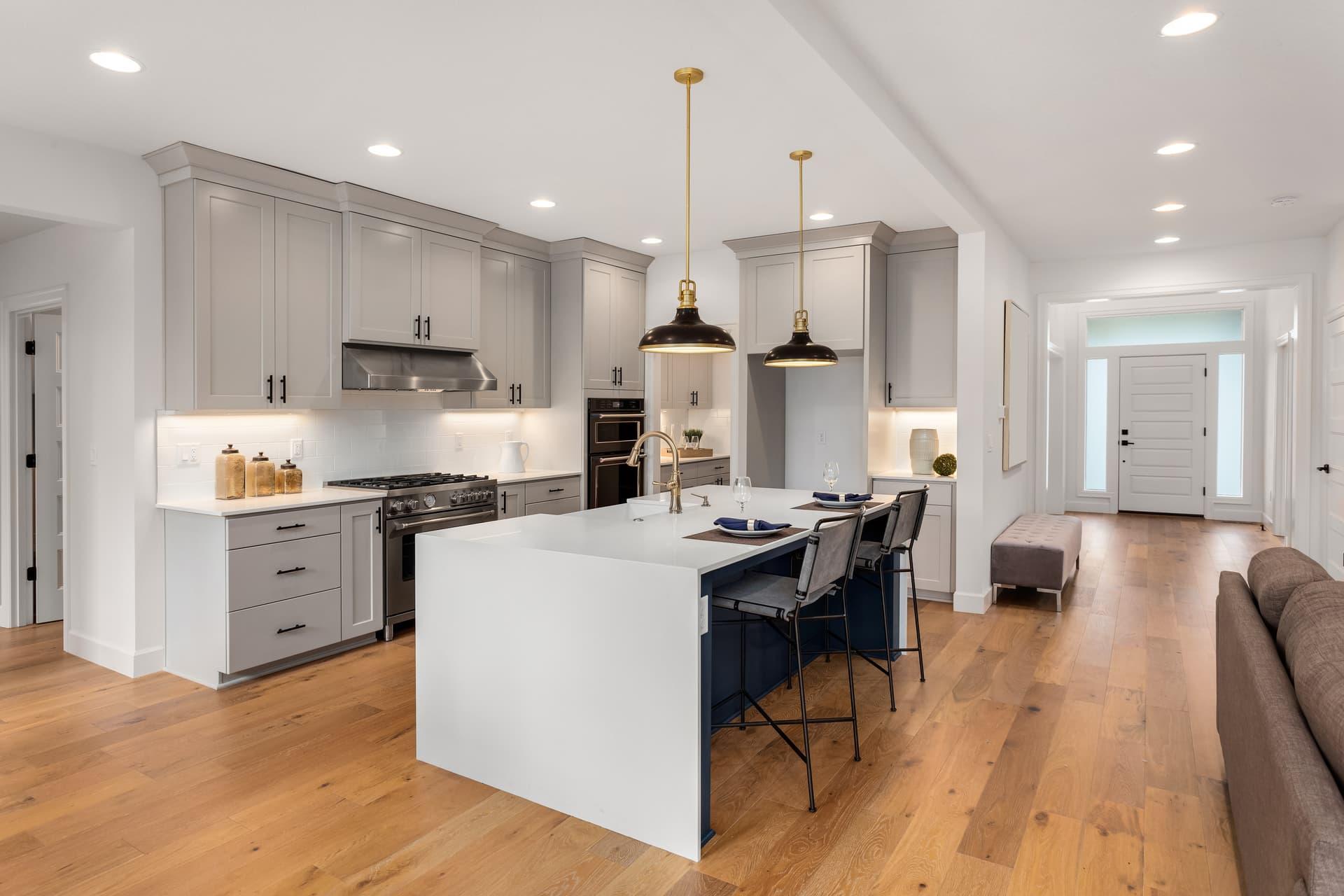 Kitchen with grey cabinets, a white waterfall island and pendant lights, open to the front entry