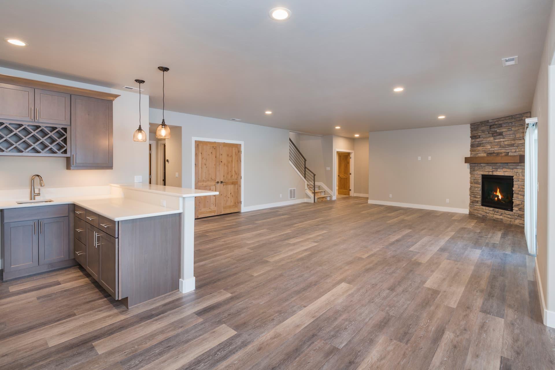 Finished basement with a grey wet bar, stone corner fireplace and wood-look plank flooring
