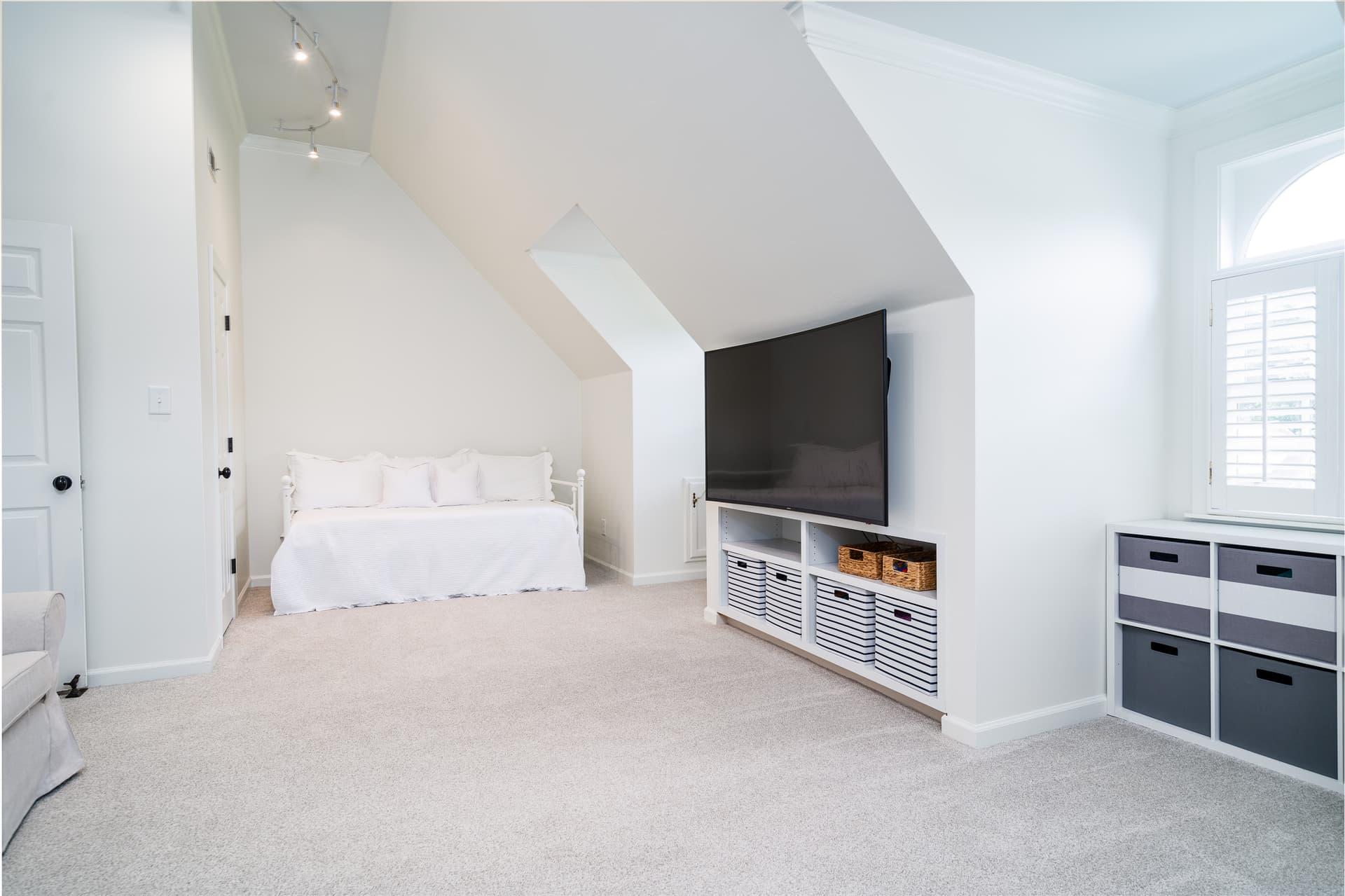 Bonus room under a sloped ceiling with a daybed, built-in storage and a wall-mounted television