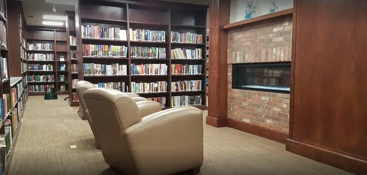 Library reading room with custom wood built-in shelving and fireplace by Can Do More
